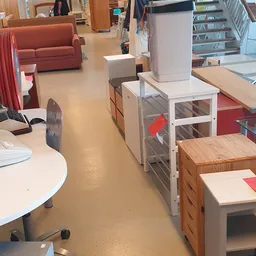 Winkelvloer met diverse meubels waaronder houten kasten, witte stellingen met grijze deuren, ronde tafels en rood/roze textie