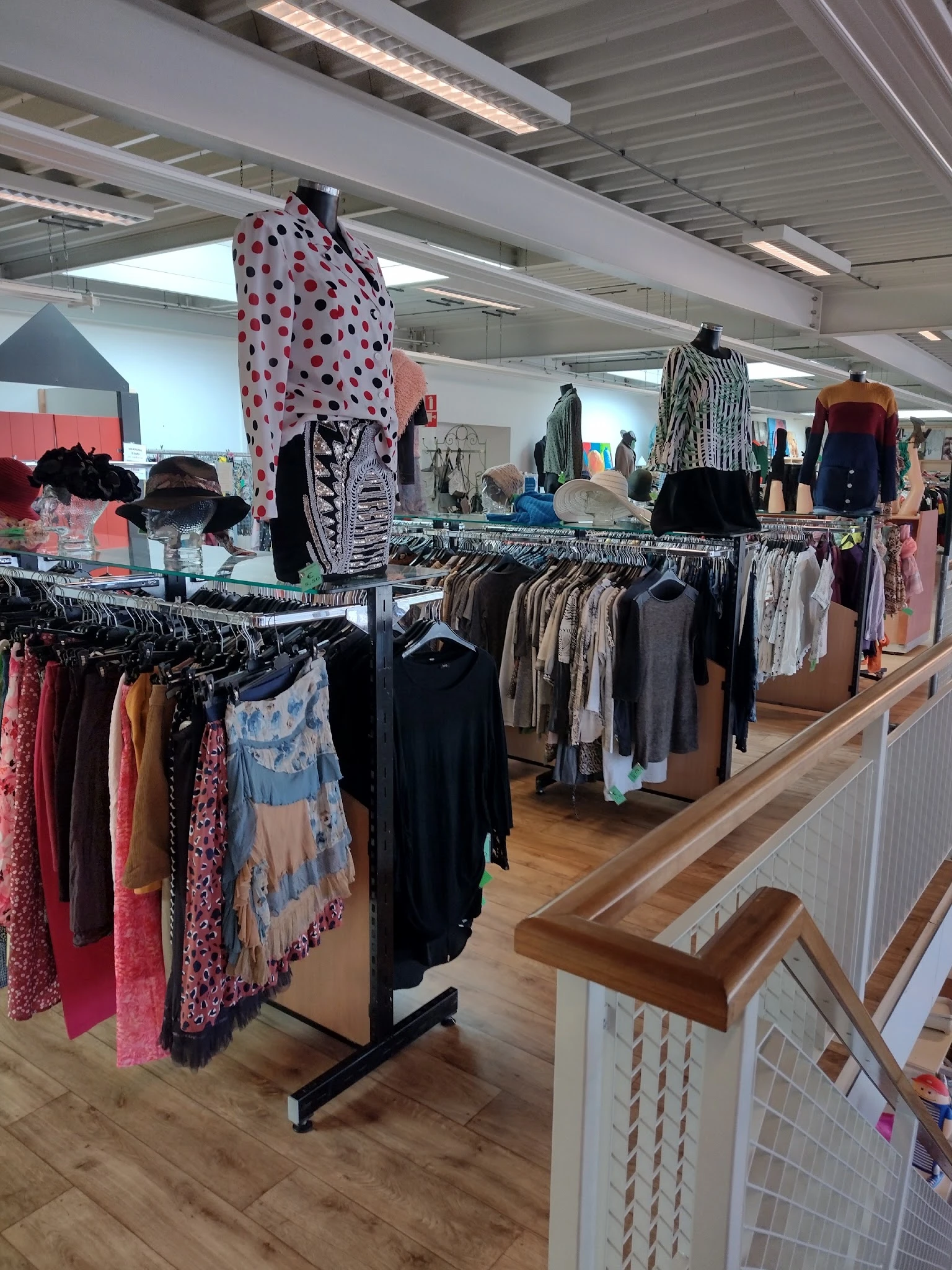 Rekken met tweedehands kleding, waaronder jurken, broeken en tops in verschillende kleuren en patronen