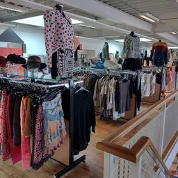 Rekken met tweedehands kleding, waaronder jurken, broeken en tops in verschillende kleuren en patronen