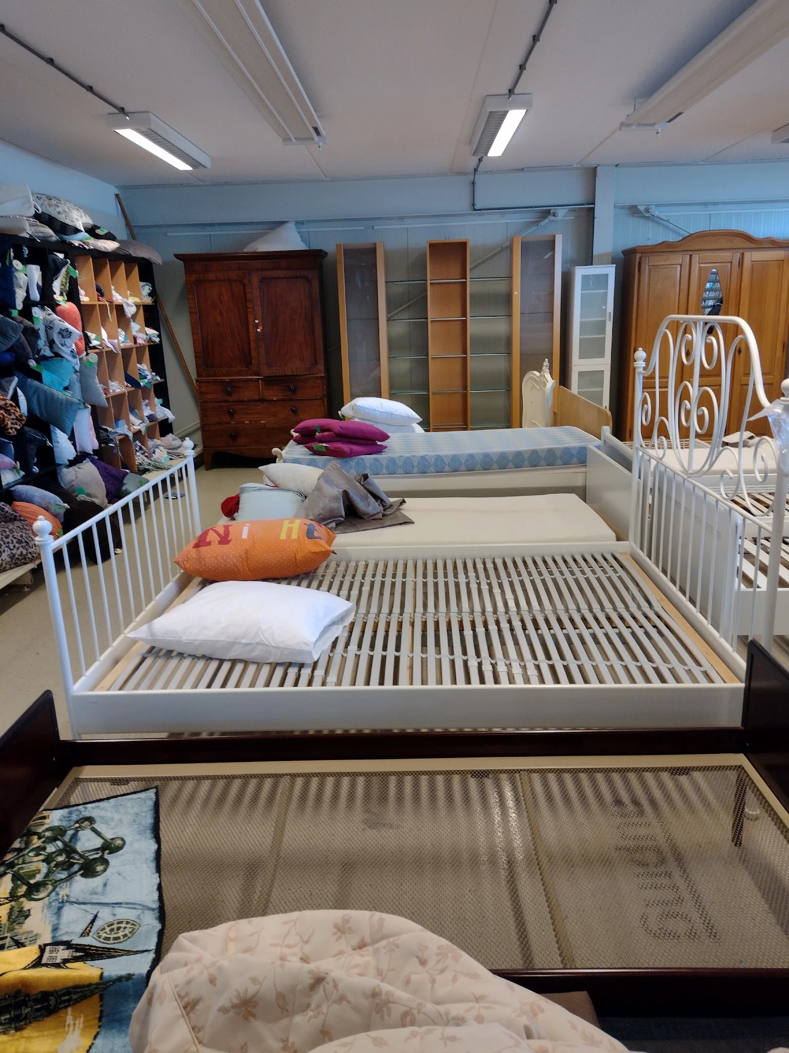 Uitgestalde bedden en matrassen in verschillende maten en kleuren met kussensets in een kringloopwinkel