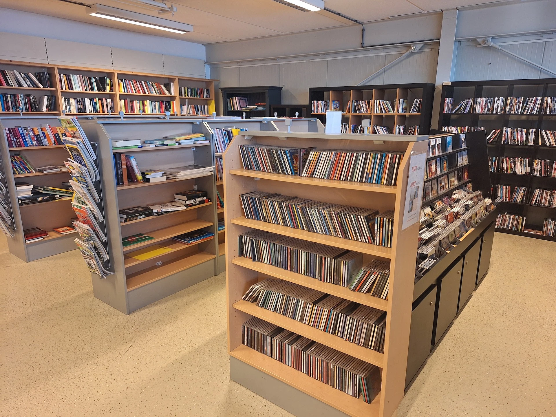 Winkelvloer met houten stellingen vol cd's en dvd's, boeken in achtergrond