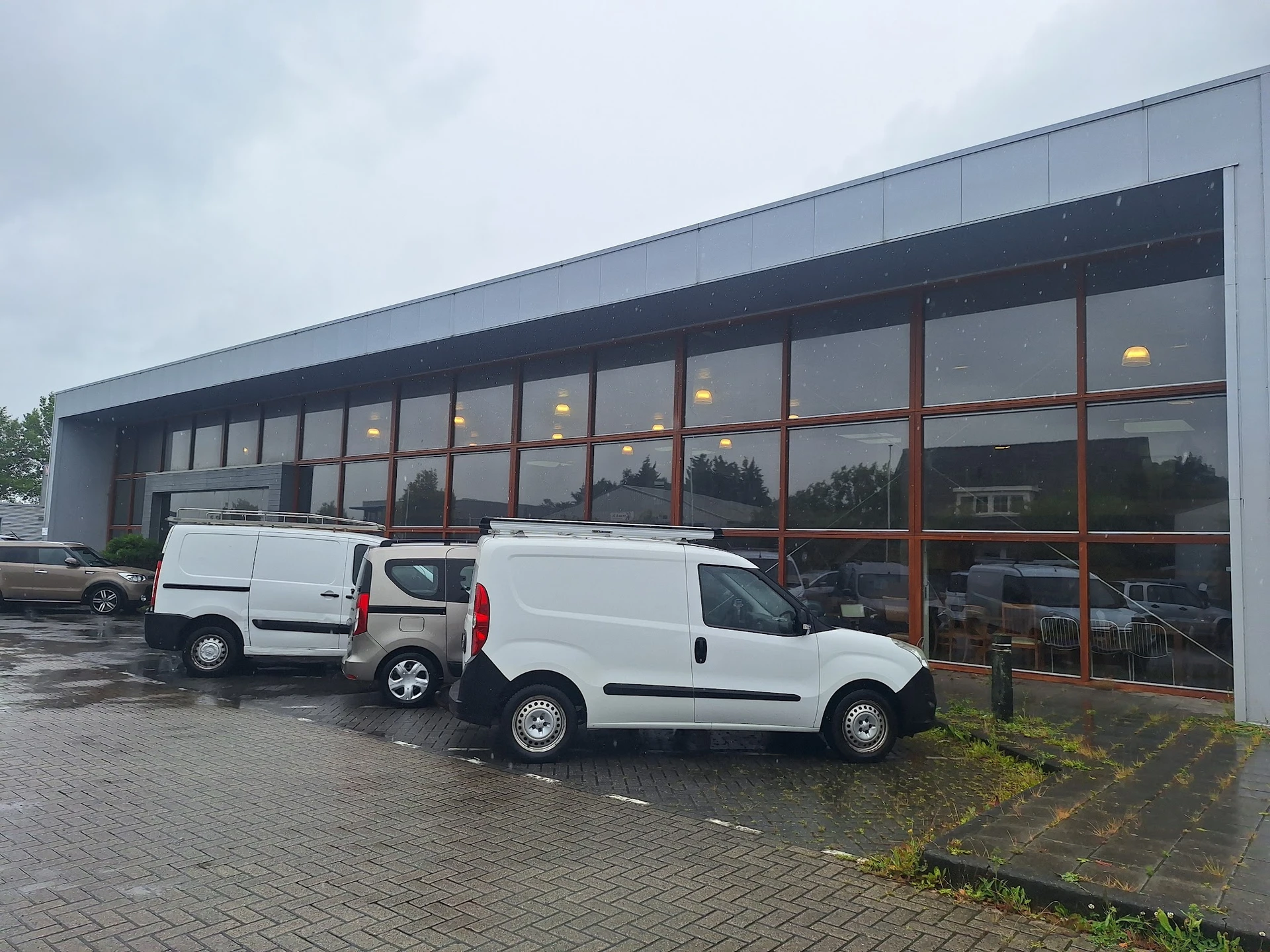 Moderne gevel van kringloopwinkel met grote ramen en twee witte bedrijfsbusjes op de parkeerplaats
