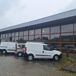 Moderne gevel van kringloopwinkel met grote ramen en twee witte bedrijfsbusjes op de parkeerplaats