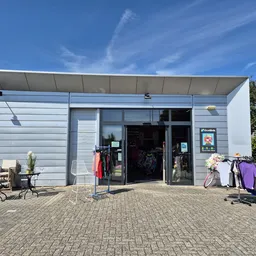 Moderne gevel van kringloopwinkel met glasdeuren, witte zijwanden en uitgestalde kleding op rekken buiten