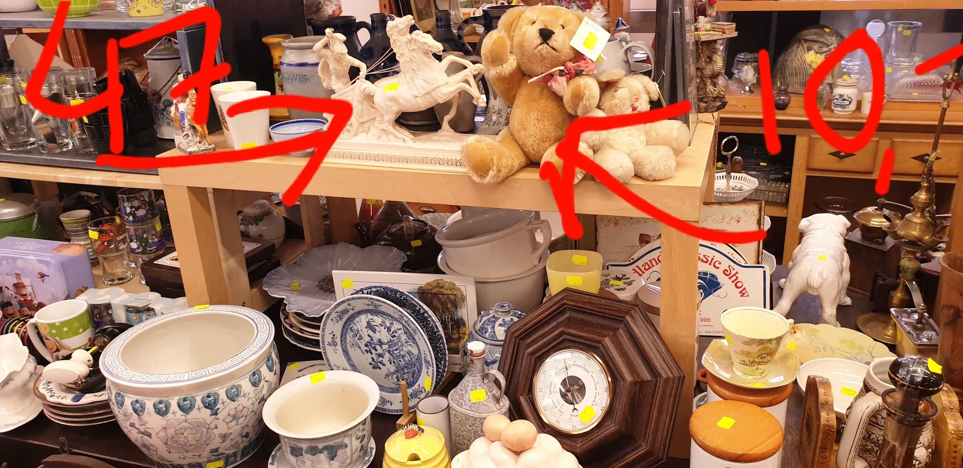 Uitgestalde tweedehands servies, kopjes, borden en knuffels op een tafel in de kringloopwinkel