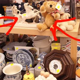 Uitgestalde tweedehands servies, kopjes, borden en knuffels op een tafel in de kringloopwinkel