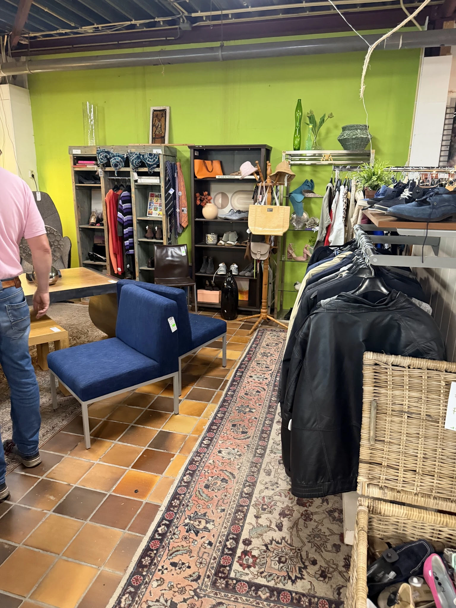 Winkelinterieur met blauwe zitbank, stellingen met kleding en spullen tegen gele wand, textile goederen en diverse artikelen