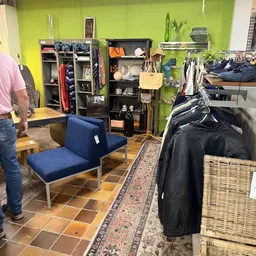 Winkelinterieur met blauwe zitbank, stellingen met kleding en spullen tegen gele wand, textile goederen en diverse artikelen