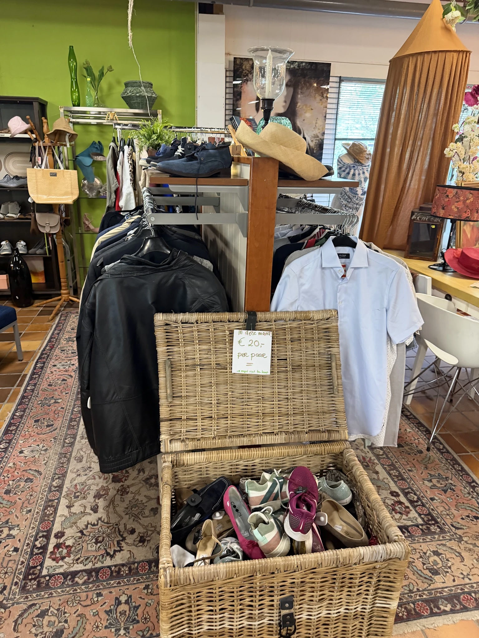 Uitgestalde tweedehands kleding en schoenen in een rieten mand met prijskaartje in een kringloopwinkel
