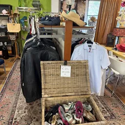 Uitgestalde tweedehands kleding en schoenen in een rieten mand met prijskaartje in een kringloopwinkel