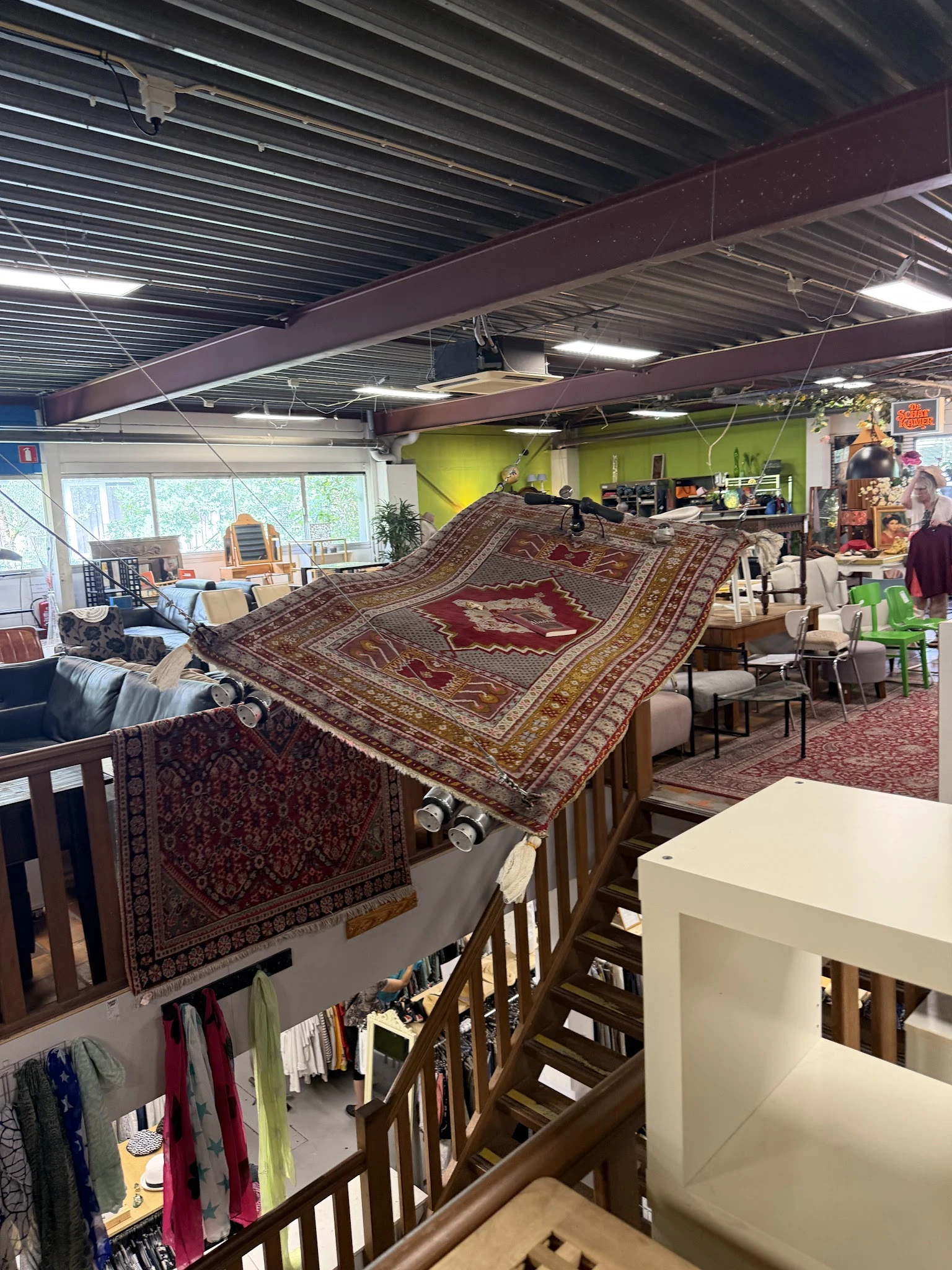Uitgestalde oosterse tapijten en vloerkleedjes in een kringloopwinkel met diverse andere spullen op de achtergrond