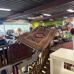 Uitgestalde oosterse tapijten en vloerkleedjes in een kringloopwinkel met diverse andere spullen op de achtergrond