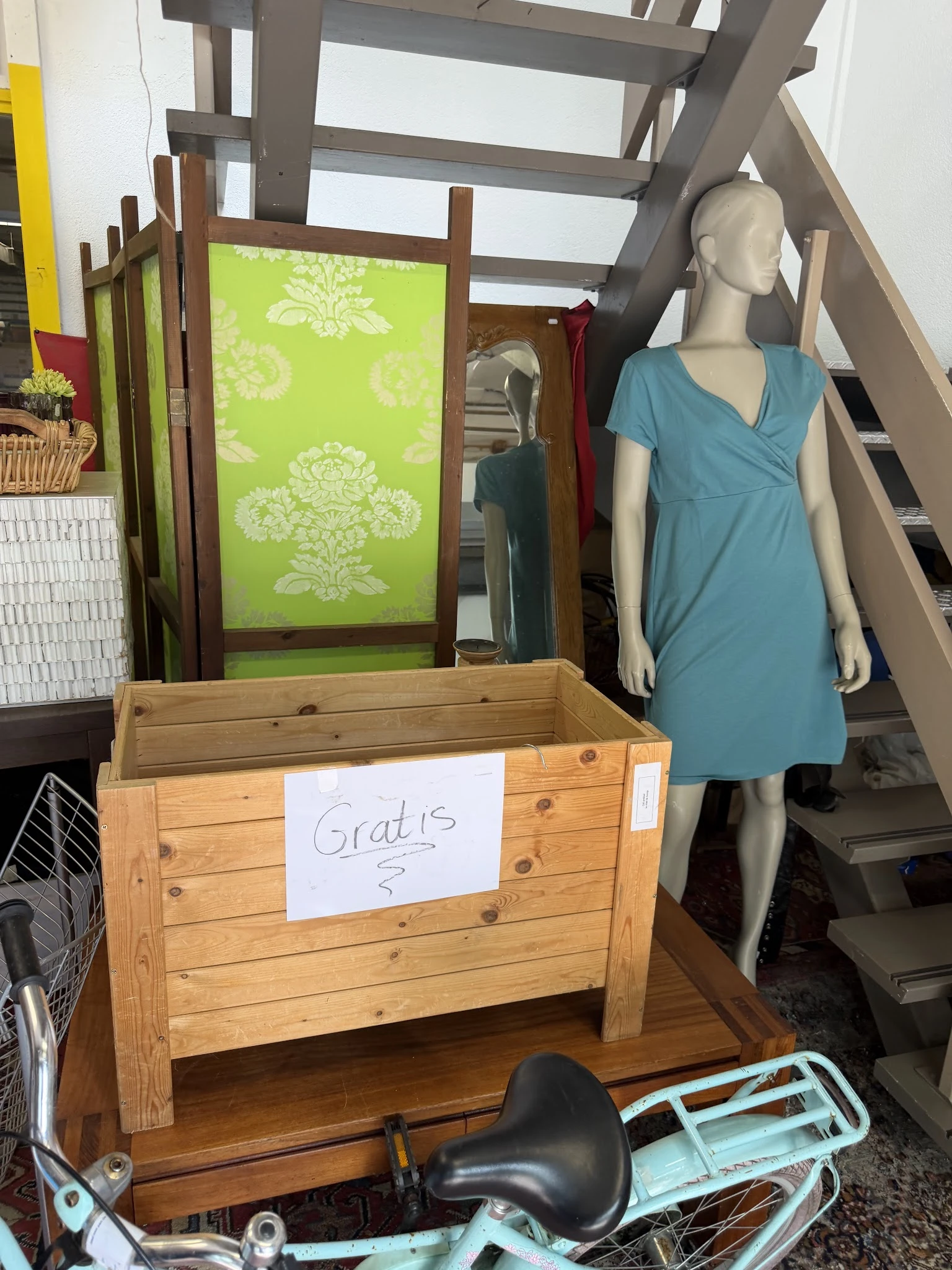 Houten kist met 'Gratis' labeltje en blauwe jurk op etalagepop in kringloopwinkel