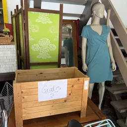 Houten kist met 'Gratis' labeltje en blauwe jurk op etalagepop in kringloopwinkel