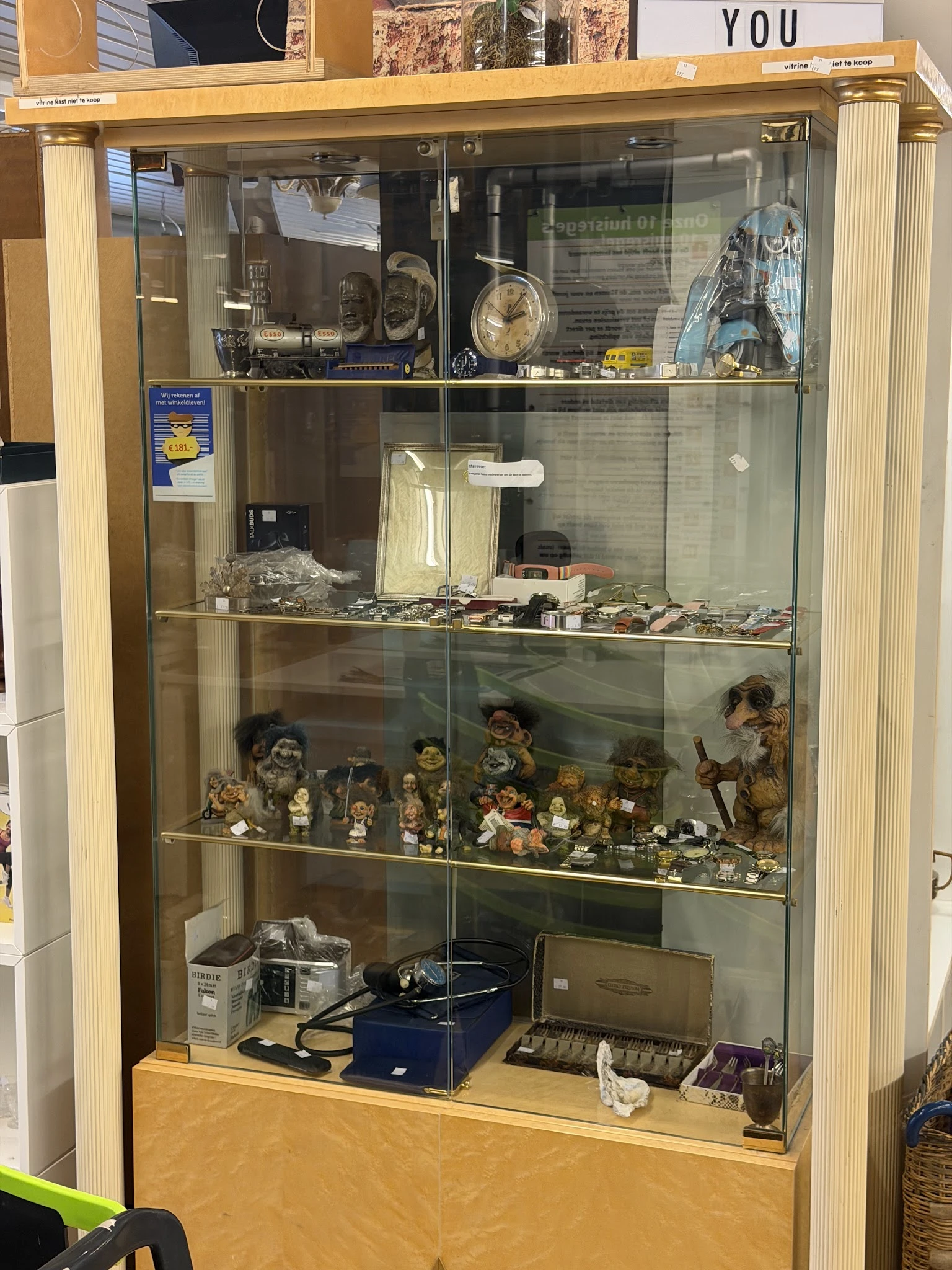 Glazen vitrinekast met diverse verzamelde beeldjes, poppen, miniatuurfiguren en decoratieve voorwerpen op meerdere niveaus