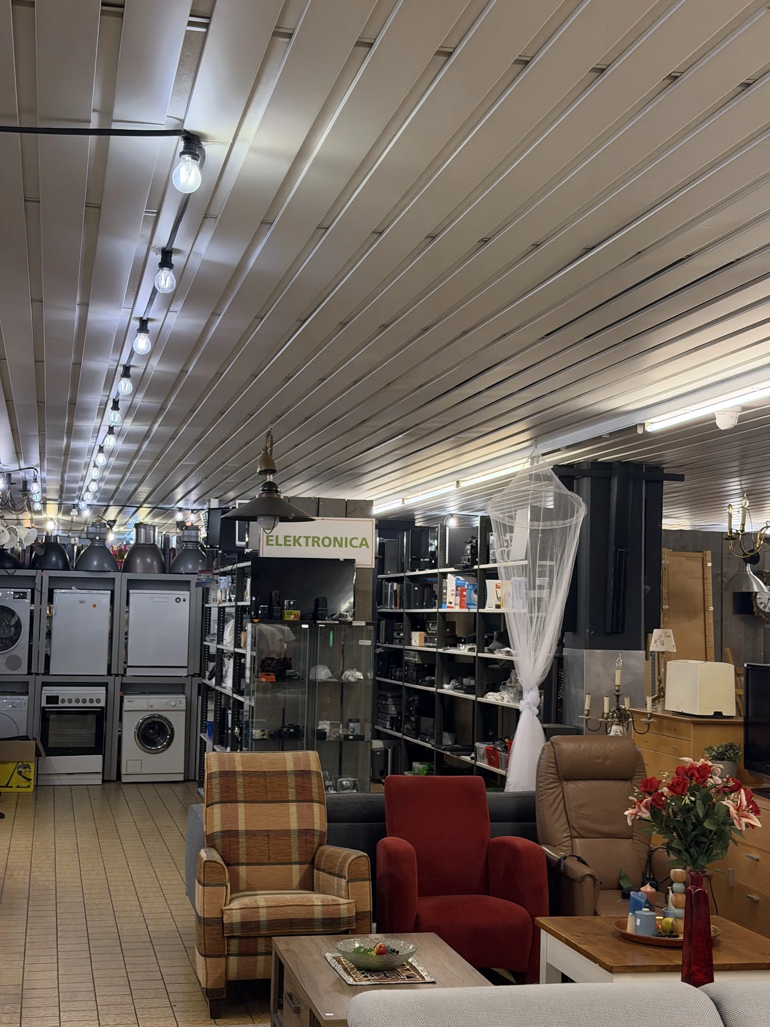 Winkelinterieur met stellingen vol elektronica en huishoudelijke apparaten, metalen plafond met ledverlichting