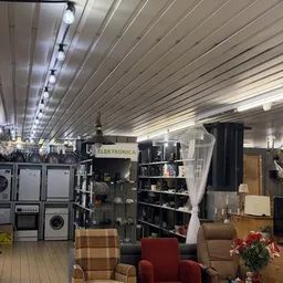 Winkelinterieur met stellingen vol elektronica en huishoudelijke apparaten, metalen plafond met ledverlichting