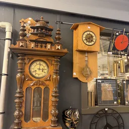 Uitgestalde houten wandklokken en klokken met slingers in de kringloopwinkel