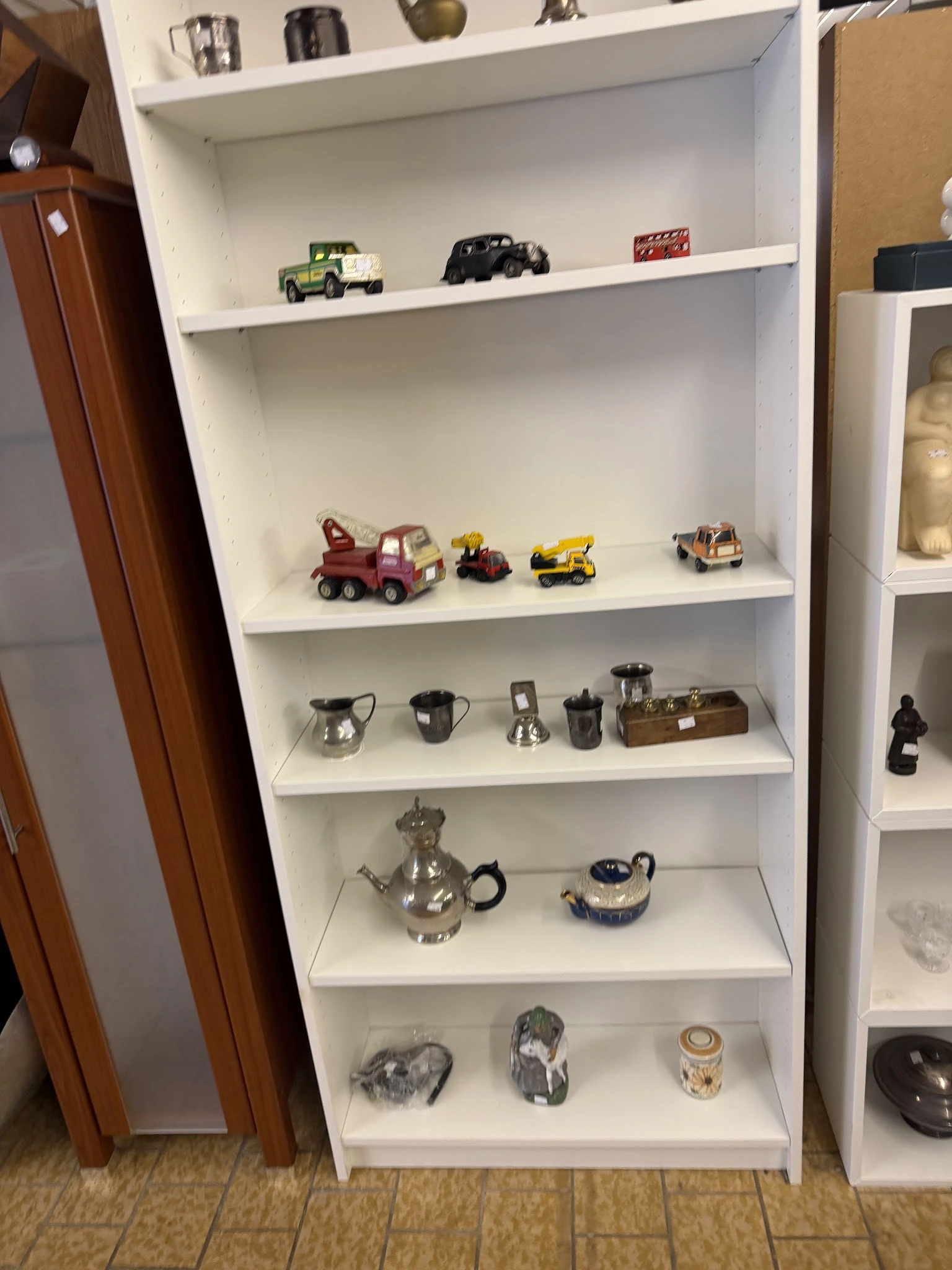 Witte wandkast met speelgoedvoertuigen, zilveren huishoudartikelen en decoratieve potten