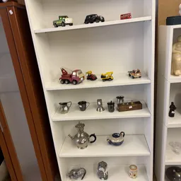 Witte wandkast met speelgoedvoertuigen, zilveren huishoudartikelen en decoratieve potten