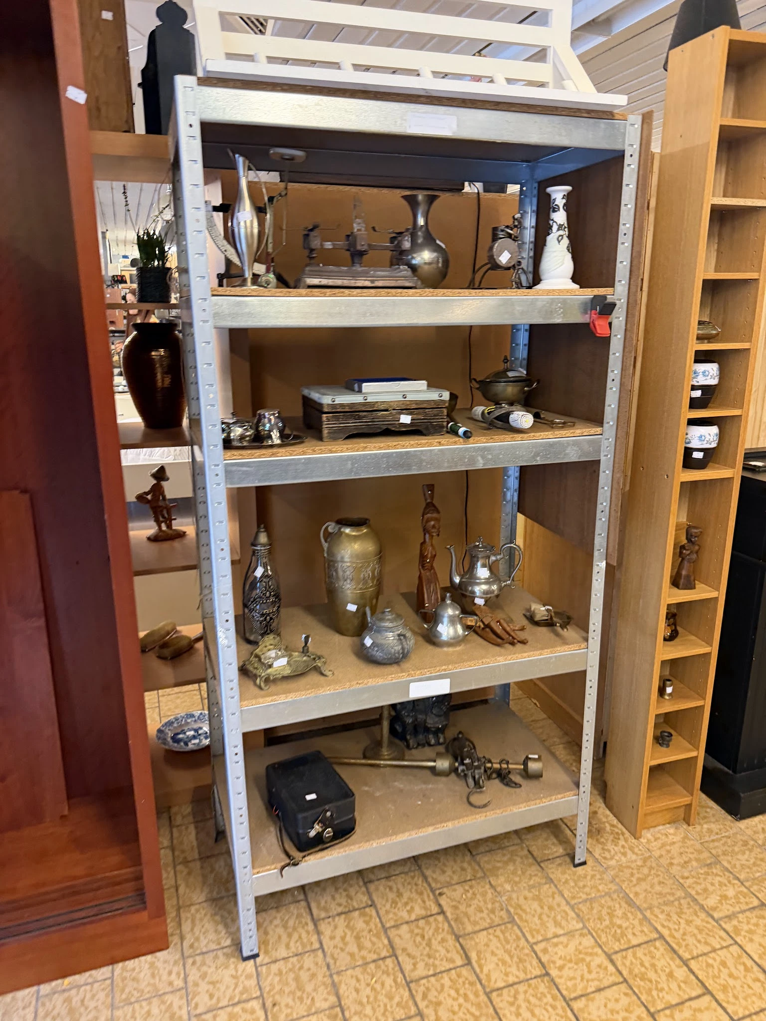 Metalen stellingkast met diverse decoratieve items zoals vazen, beeldjes, kandelaars en kunstobjecten op verschillende niveau
