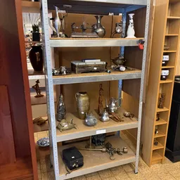 Metalen stellingkast met diverse decoratieve items zoals vazen, beeldjes, kandelaars en kunstobjecten op verschillende niveau