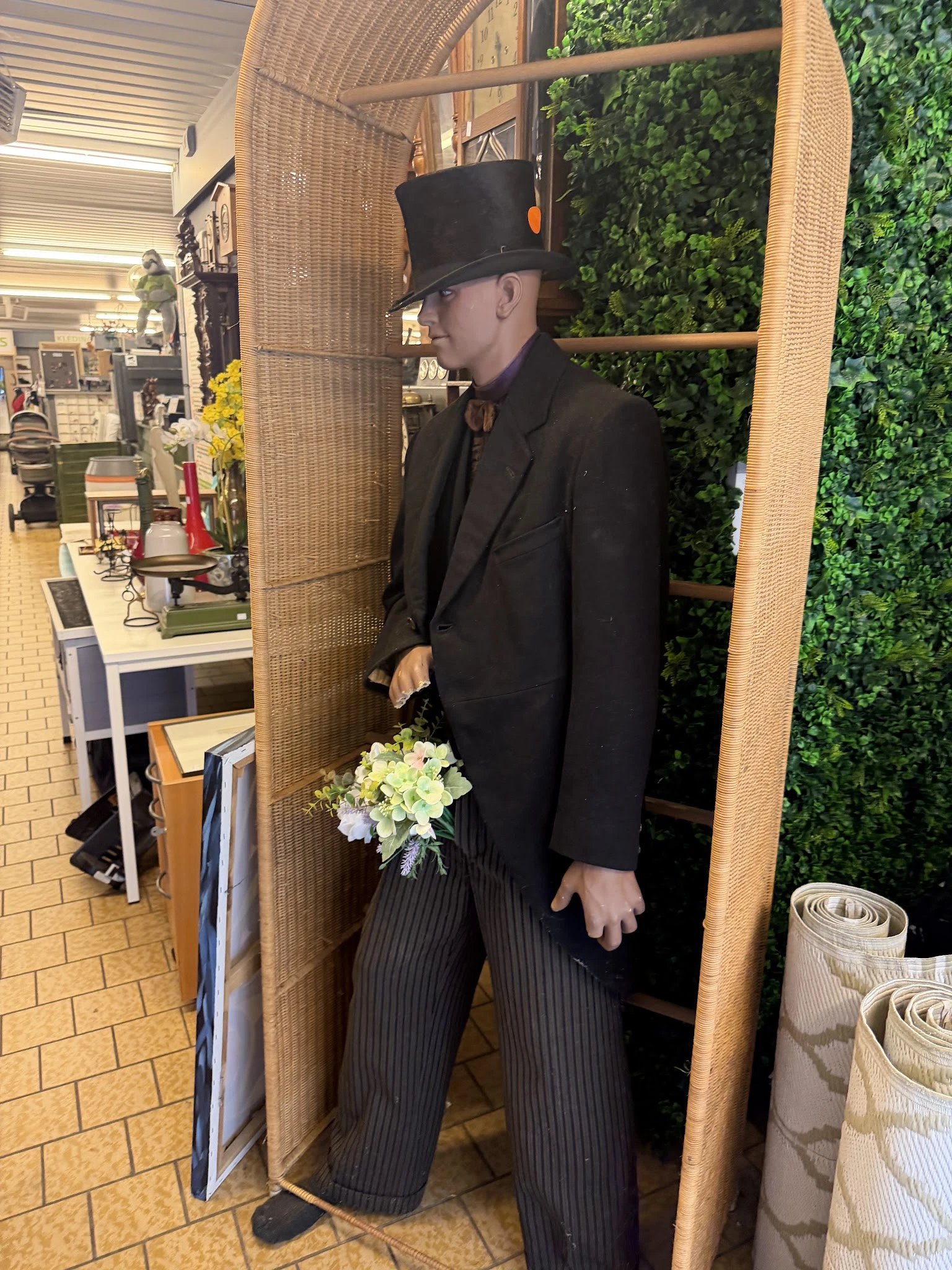 Mannequin in zwart pak met hoed en wit bloemstuk in de hand