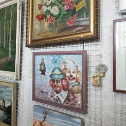 Aan muur opgehangen schilderijen en decoratieve items waaronder een portret van twee clowns en een glazen bol