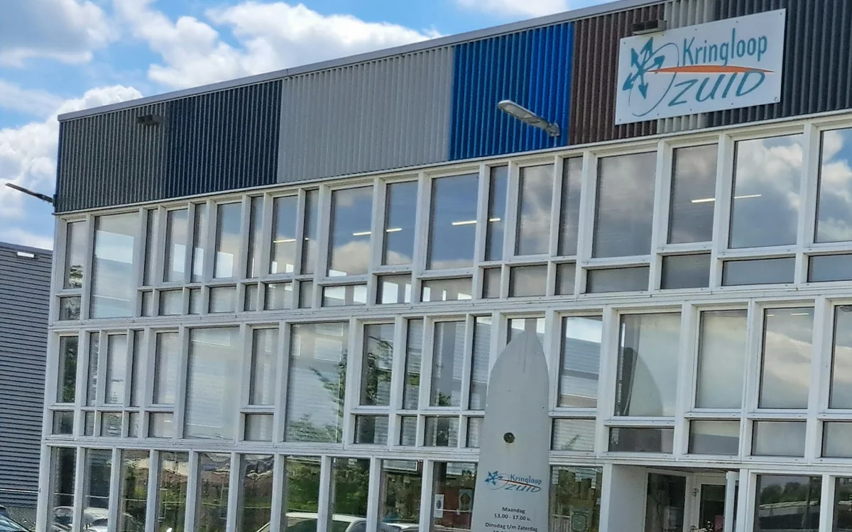 Grijze gevel met grote ramen en blauwe accenten, winkelnaam Kringloop Zuid zichtbaar op bord