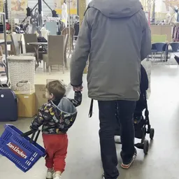 Volwassene en klein kind in winkelkledingafdeling met winkelwagen
