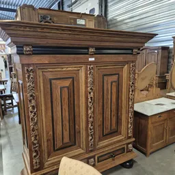Antieke houten kast met geornamenteerde deuren en decoratieve zijpanelen in kringloopwinkel