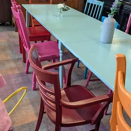 Eettafel met lichtblauwe blad en gekleurde stoelen in roze, rood en oranje in de winkelruimte