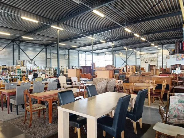Ruime winkelhal met diverse meubels, tafels en stoelen uitgestald onder industrieel plafond met spotverlichting