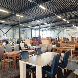 Ruime winkelhal met diverse meubels, tafels en stoelen uitgestald onder industrieel plafond met spotverlichting