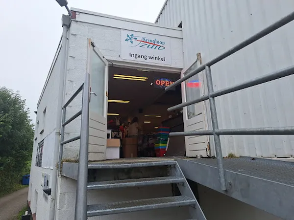 Ingang van een kringloopwinkel in een zilvergrijze containerwagen met openstaande deuren en verlichte binnenkant