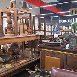 Houten meubels en decoratieve objecten uitgestald in de kringloopwinkel, met tafels, stoelen en beeldjes