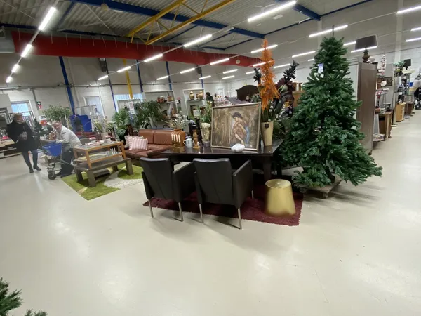 Winkelvloer met diverse meubelstukken zoals zithoeken, tafels en decoratieve objecten, met planten en verlichte plafondconstr