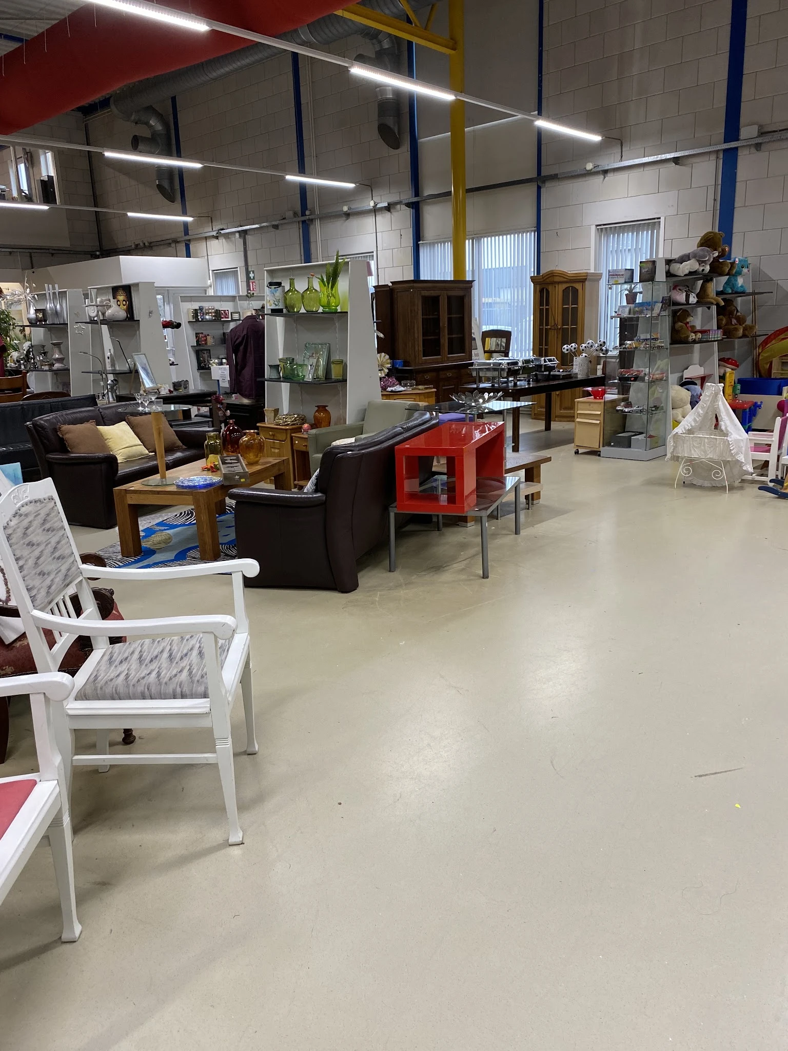 Winkelvloer met diverse meubels: zwarte fauteuils, rode tafel, witte stoelen en houten kasten op de achtergrond