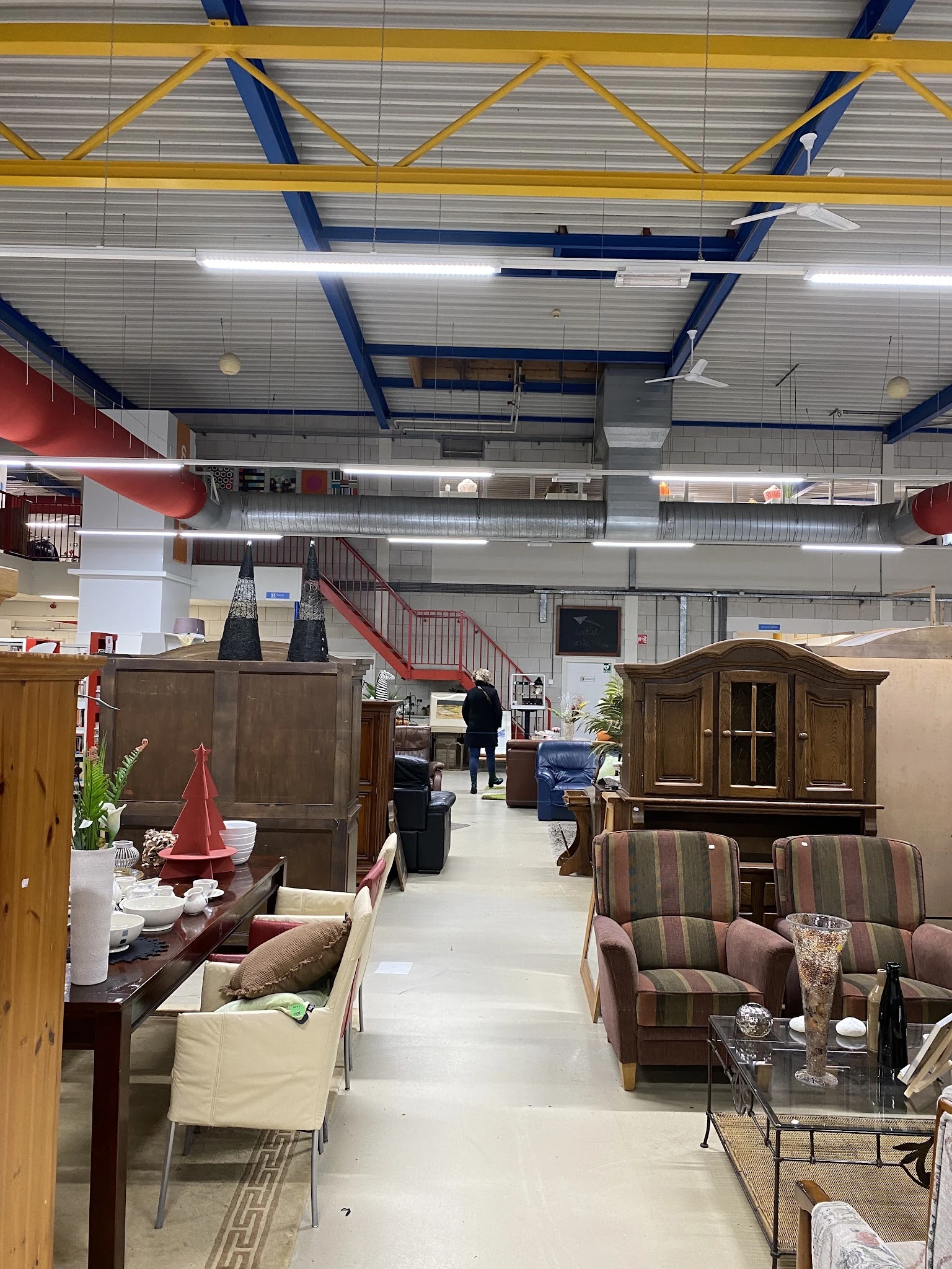 Winkelvloer met meubels uitgestald: kasten, fauteuils en ander meubilair onder industrieel plafond met blauwe buizen