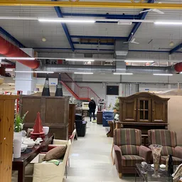Winkelvloer met meubels uitgestald: kasten, fauteuils en ander meubilair onder industrieel plafond met blauwe buizen