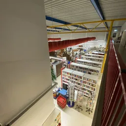 Overzicht van kringloopwinkel met boekenrekken, stellingen met diverse artikelen en geel geraamte aan plafond