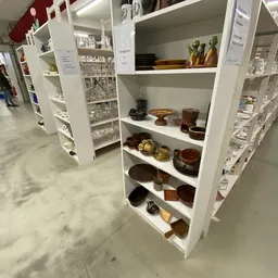 Witte stellingkasten met tweedehands servies, kommen, kannen en decoratieve items in bruine en gouden tinten