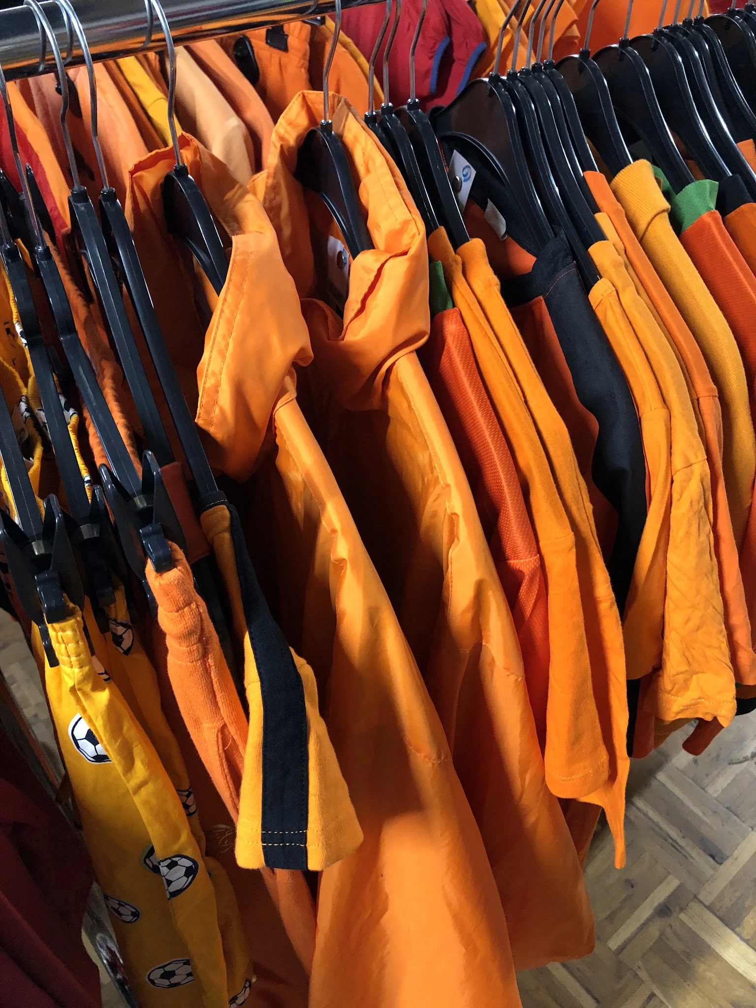 Rekken met kleurige tweedehands kleding in oranje, geel en marineblauw tinten