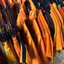 Rekken met kleurige tweedehands kleding in oranje, geel en marineblauw tinten