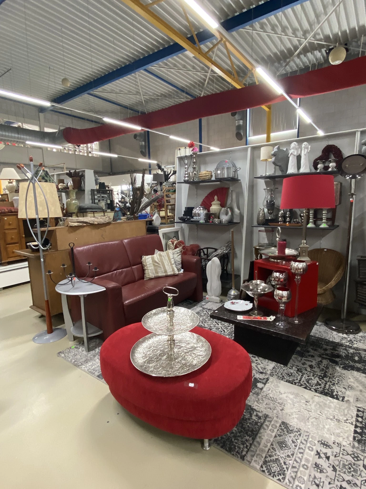 Ingerichte woonkamer display met bordeauxrode bank, tafels en decoratieve items in een kringloopwinkel