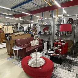 Ingerichte woonkamer display met bordeauxrode bank, tafels en decoratieve items in een kringloopwinkel