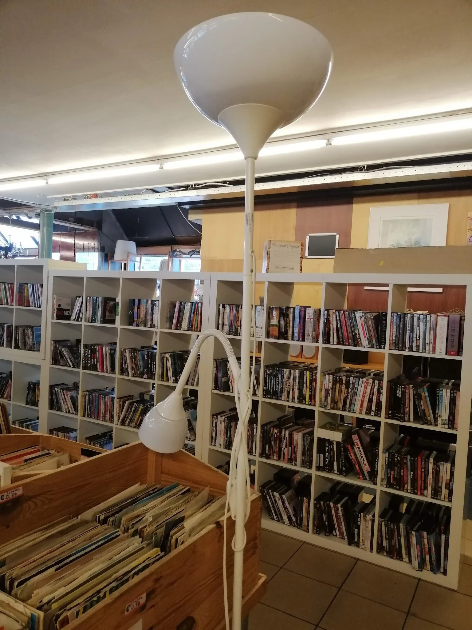 Boekenrekken vol boeken in een kringloopwinkel, wit steelframe met houder, geel en terracotta gekleurde muren.