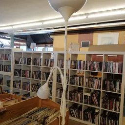 Boekenrekken vol boeken in een kringloopwinkel, wit steelframe met houder, geel en terracotta gekleurde muren.