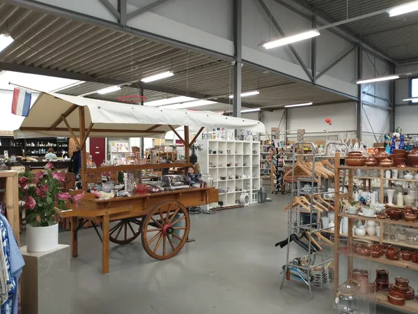 Ruim winkelinterieur met diverse tweedehands spullen, meubels, stellingen en decoratieve items op grijze vloer