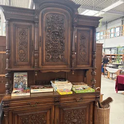 Antieke houten kast met ornamentale snijwerk, gevuld met boeken op de onderste plank